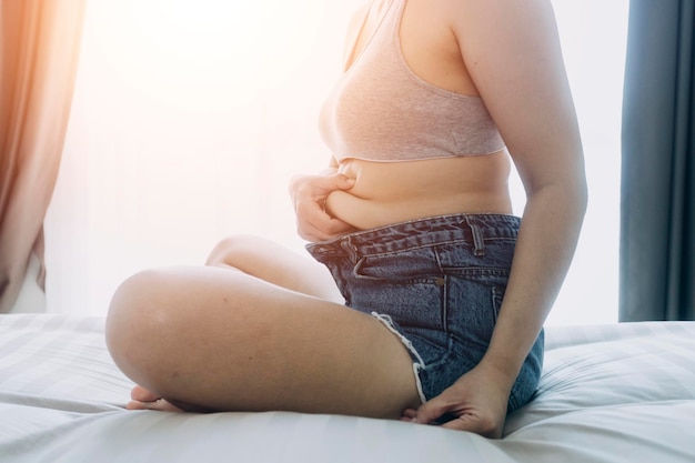 Linda mulher gorda com fita métrica Ela usa a mão para espremer o excesso de gordura que está isolado em um fundo branco Ela quer perder peso o conceito de cirurgia e quebrar a gordura sob o