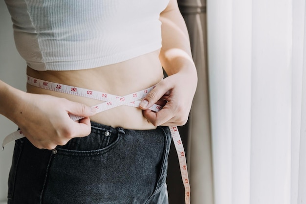 Linda mulher gorda com fita métrica Ela usa a mão para espremer o excesso de gordura que está isolado em um fundo branco Ela quer perder peso o conceito de cirurgia e quebrar a gordura sob o