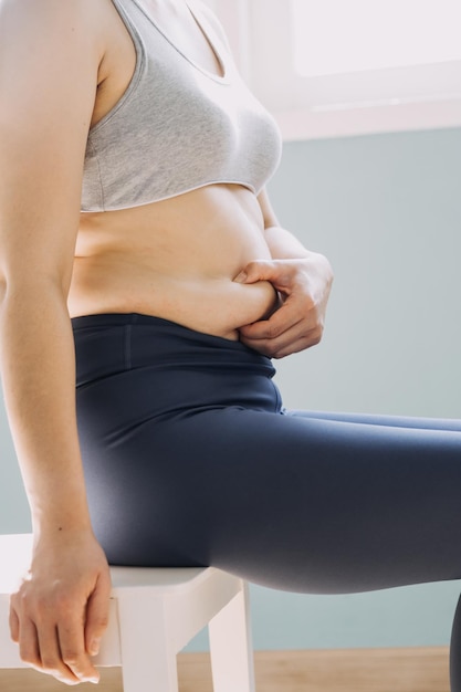 Linda mulher gorda com fita métrica Ela usa a mão para espremer o excesso de gordura que está isolado em um fundo branco Ela quer perder peso o conceito de cirurgia e quebrar a gordura sob o