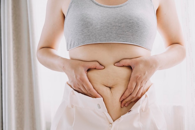 Linda mulher gorda com fita métrica Ela usa a mão para espremer o excesso de gordura que está isolado em um fundo branco Ela quer perder peso o conceito de cirurgia e quebrar a gordura sob o