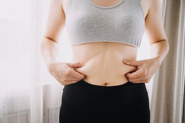 Linda mulher gorda com fita métrica Ela usa a mão para espremer o excesso de gordura que está isolado em um fundo branco Ela quer perder peso o conceito de cirurgia e quebrar a gordura sob o