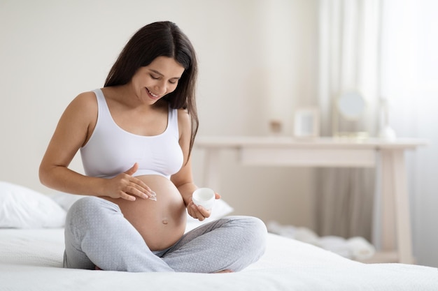 Linda mulher grávida aplicando creme corporal em sua barriga grande