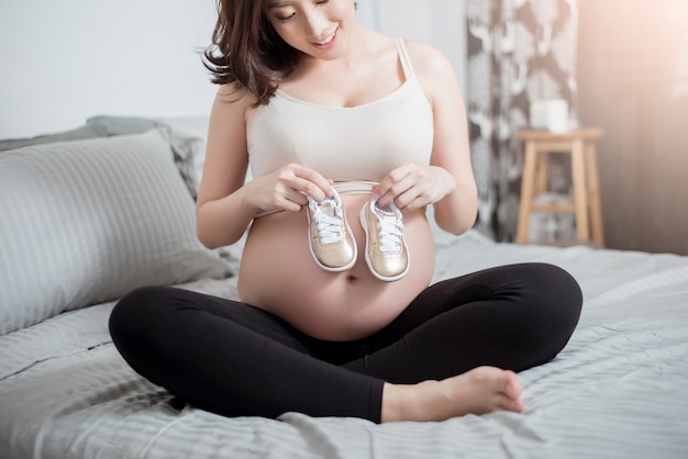 Linda mulher grávida asiática esperando seu bebê com sapatos pequenos