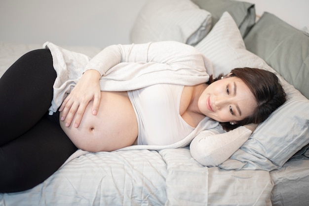 Linda mulher grávida asiática está dormindo na cama