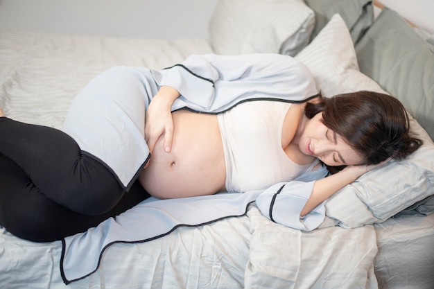 Foto linda mulher grávida asiática está dormindo na cama