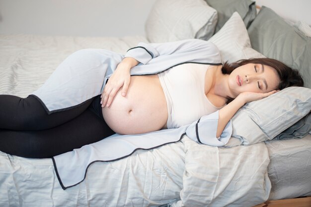 Linda mulher grávida asiática está dormindo na cama