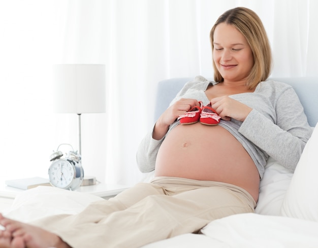 Linda mulher grávida colocando sapatos de bebê em sua barriga