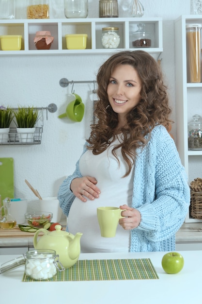 Linda mulher grávida com chá na cozinha