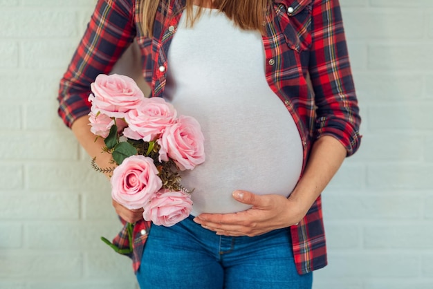 Linda mulher grávida com flores de tulipas segura as mãos na barriga em fundo branco.