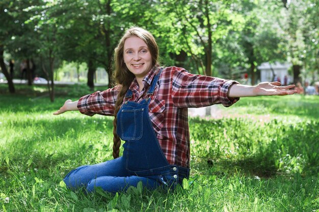 Linda mulher grávida de macacão jeans sentado na grama do parque