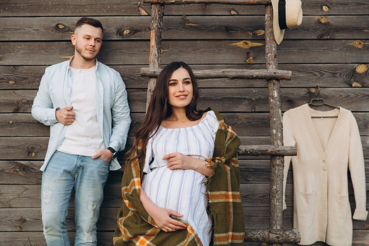 Foto linda mulher grávida e o marido posando perto de prédio de madeira. elegante casal feliz se amam. moda e estilo rústico.