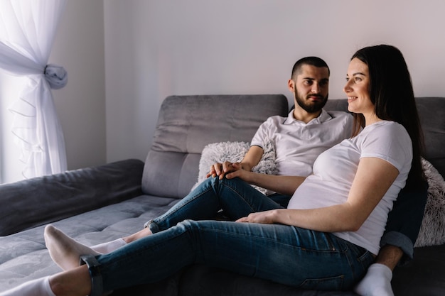 Linda mulher grávida e seu belo marido estão sorrindo enquanto passam tempo juntos na cama o homem está ouvindo o bebê na barriga