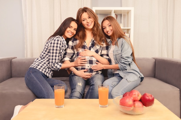 Linda mulher grávida e suas amigas felizes sentadas no sofá