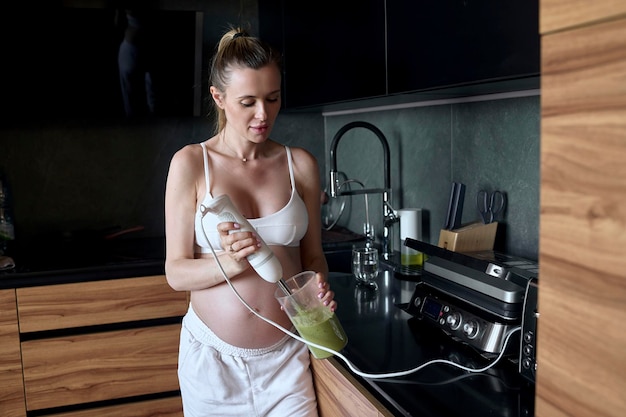 Linda mulher grávida fazendo smoothies de frutas com liquidificador H