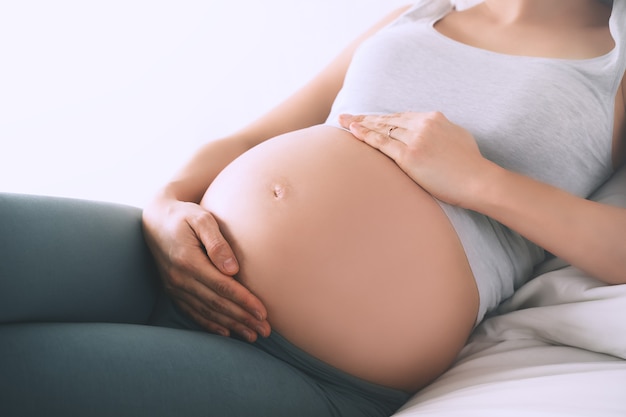 linda mulher grávida relaxada de mãos dadas na barriga no quarto em casa