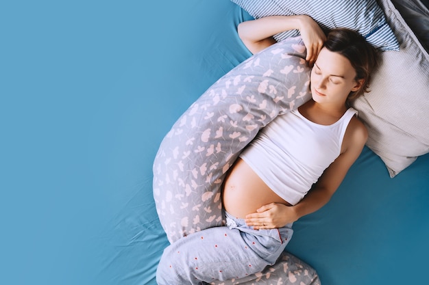 linda mulher grávida relaxando ou dormindo com almofada de apoio de barriga na cama conceito de gravidez
