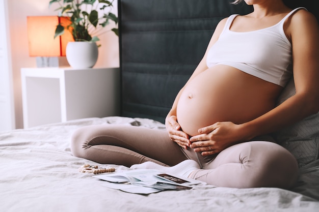 Linda mulher grávida segurando a barriga com as mãos no quarto em casa