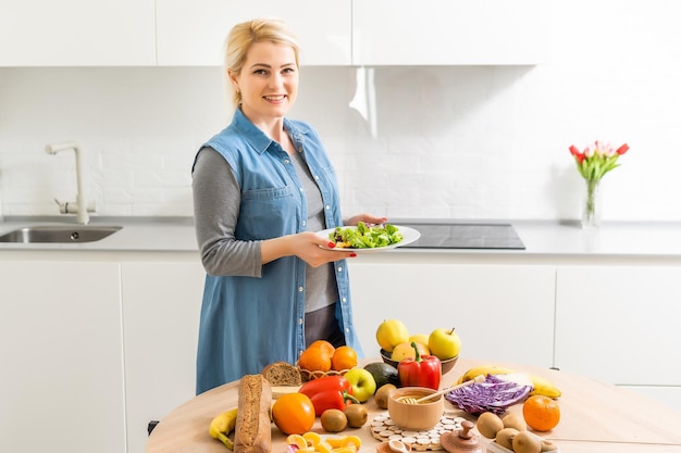 Linda mulher grávida sorrindo com comida saudável de legumes na cozinha. Conceito de comida saudável.
