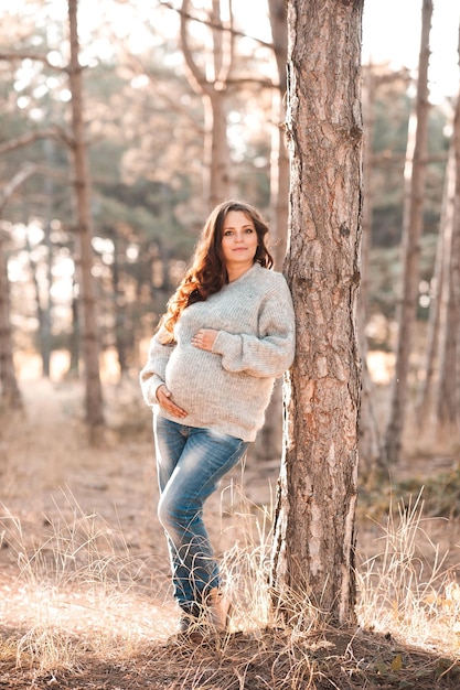 Linda mulher grávida usa cardigã de malha posando ao ar livre na floresta