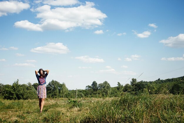 Linda mulher hipster andando no campo verde de verão no fundo do espaço do céu azul para texto