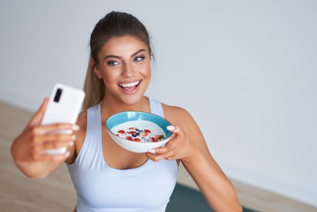 linda mulher hispânica comendo iogurte e segurando um smartphone, promovendo um estilo de vida saudável e fazendo dieta