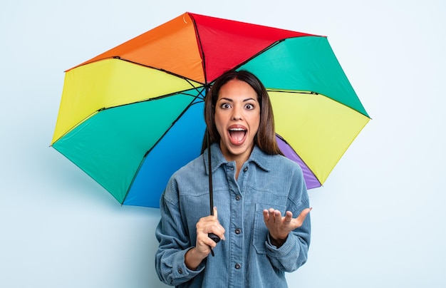 Linda mulher hispânica espantada, chocada e atônita com uma surpresa inacreditável. conceito de guarda-chuva