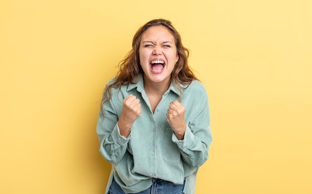 Linda mulher hispânica gritando agressivamente com olhar irritado, frustrado e irritado e punhos cerrados, sentindo-se furiosa