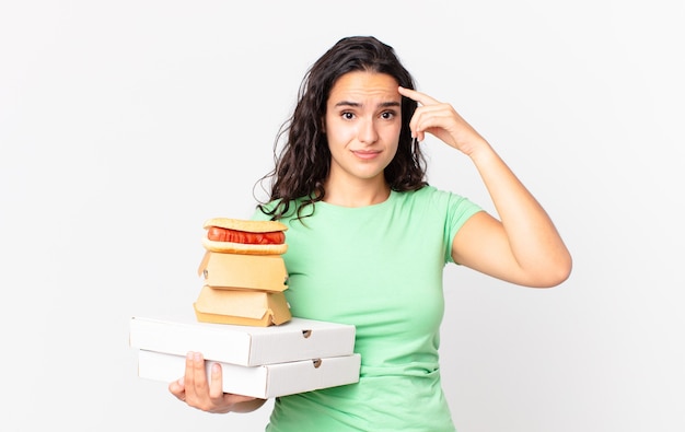 Linda mulher hispânica se sentindo confusa e perplexa, mostrando que você é maluco e segurando caixas de comida rápida