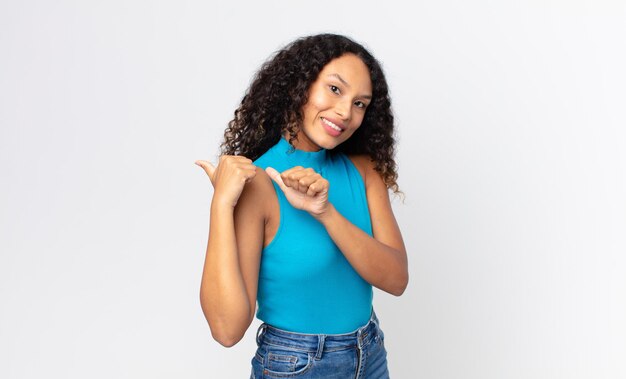 Linda mulher hispânica sorrindo alegre e casualmente apontando para uma cópia do espaço ao lado, sentindo-se feliz e satisfeita