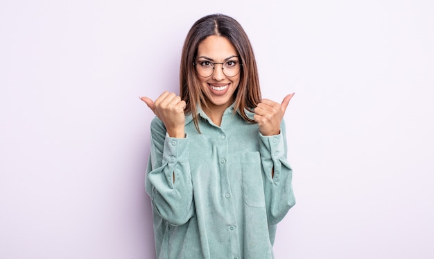 Linda mulher hispânica sorrindo alegremente e parecendo feliz, sentindo-se despreocupada e positiva com os dois polegares para cima