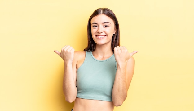 Linda mulher hispânica sorrindo com alegria e parecendo feliz, sentindo-se despreocupada e positiva com os dois polegares para cima