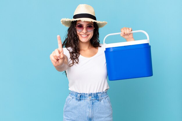 Linda mulher hispânica sorrindo com orgulho e confiança em primeiro lugar segurando uma geladeira portátil