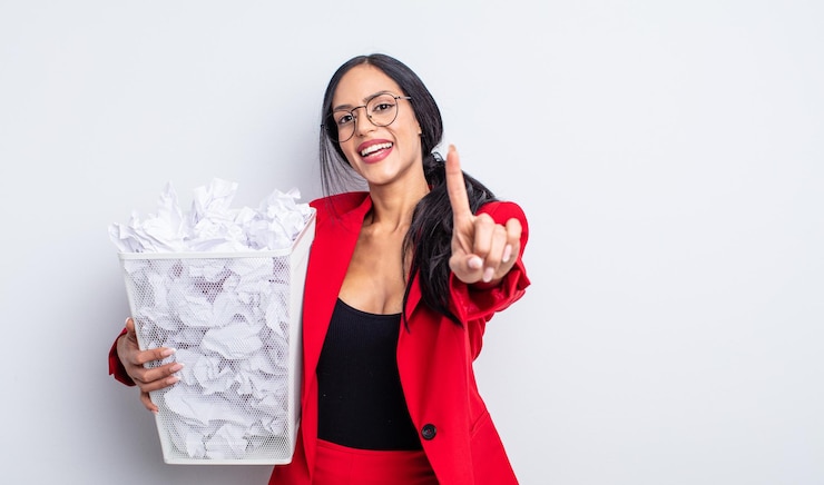 Foto linda mulher hispânica sorrindo com orgulho e confiança fazendo o conceito número um de lixo de bolas de papel