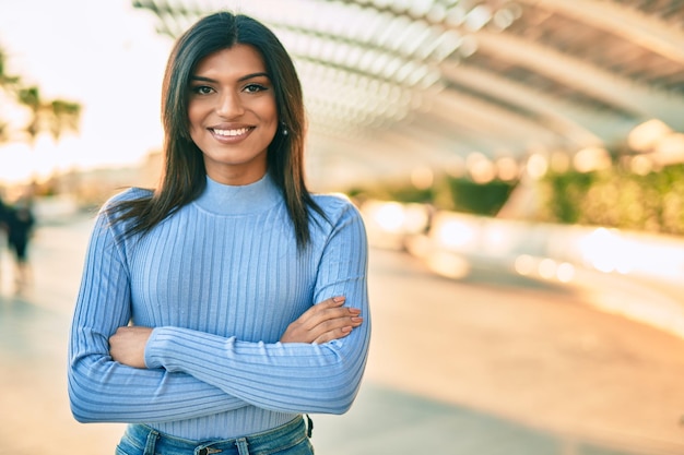 Linda mulher hispânica sorrindo confiante com os braços cruzados na cidade