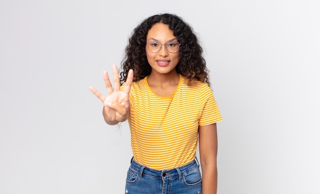 Linda mulher hispânica sorrindo e parecendo amigável, mostrando o número quatro ou o quarto com a mão para a frente, em contagem regressiva