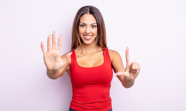 Linda mulher hispânica sorrindo e parecendo amigável, mostrando o número sete ou sétimo com a mão para a frente, em contagem regressiva