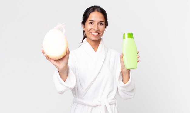 Linda mulher hispânica usando roupão de banho e segurando um shampoo e uma esponja