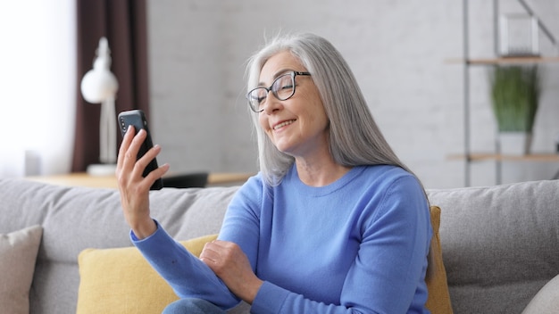 Linda mulher idosa de cabelos grisalhos sorrindo usando smartphone