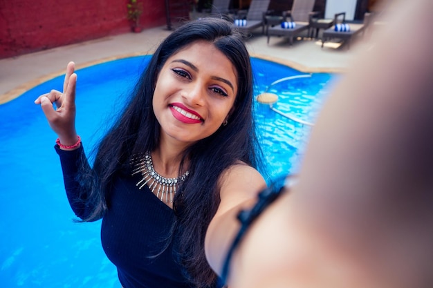 Linda mulher indiana, sorriso branco, retrato de selfie na câmera do smartphone, café de verão à beira-mar, perto da piscina goa