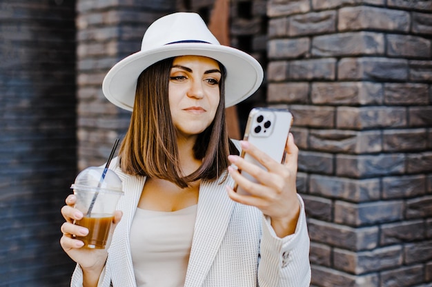 Linda mulher indo ao encontro com café frio e segurando o telefone andando na rua