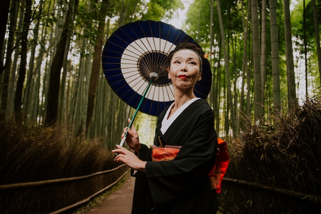 Linda mulher japonesa sênior andando na floresta de bambu