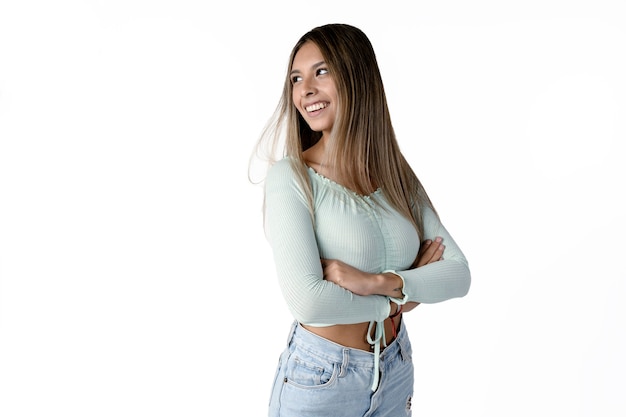 Linda mulher latina com os braços cruzados em pé de lado, olhando sorrindo para o lado com fundo branco puro.