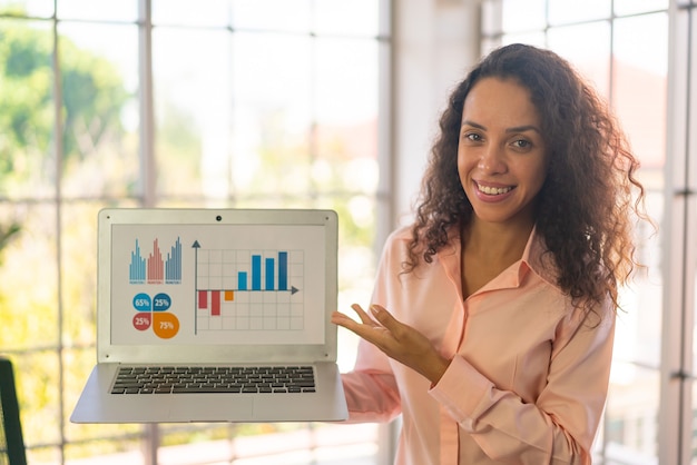 Foto linda mulher latina mostrando laptop com gráfico de negócios na tela