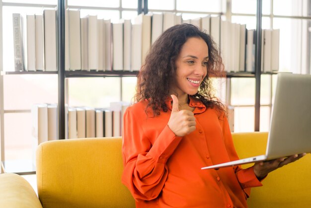 Linda mulher latina trabalhando com laptop no sofá com sentimento feliz