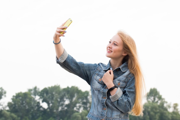 Linda mulher loira com cabelo comprido e jeans com um sorriso faz uma selfie