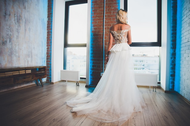 Linda mulher loira com cabelos longos, vestido com ombros nus, posando na janela.