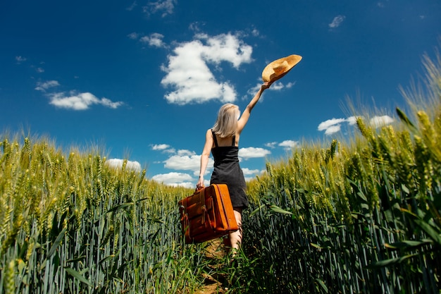 Linda mulher loira com mala no campo de trigo em dia de sol