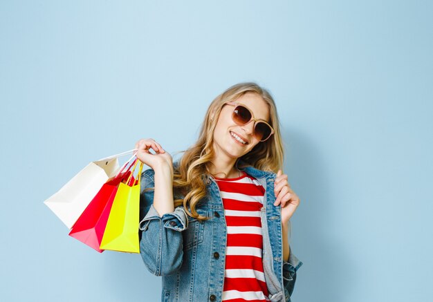 Linda mulher loira com óculos de sol gosta de fazer compras no fundo azul