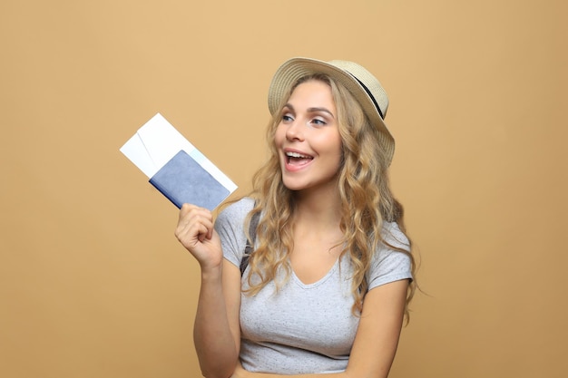 Foto linda mulher loira com roupas de verão, posando com passaporte com ingressos sobre fundo bege.