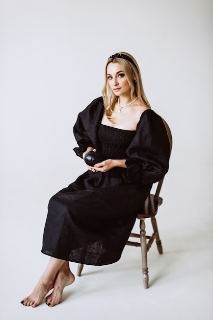 Linda mulher loira com vestido de linho preto com uma abóbora nas mãos. Moda étnica, tecido natural. Foco seletivo suave.